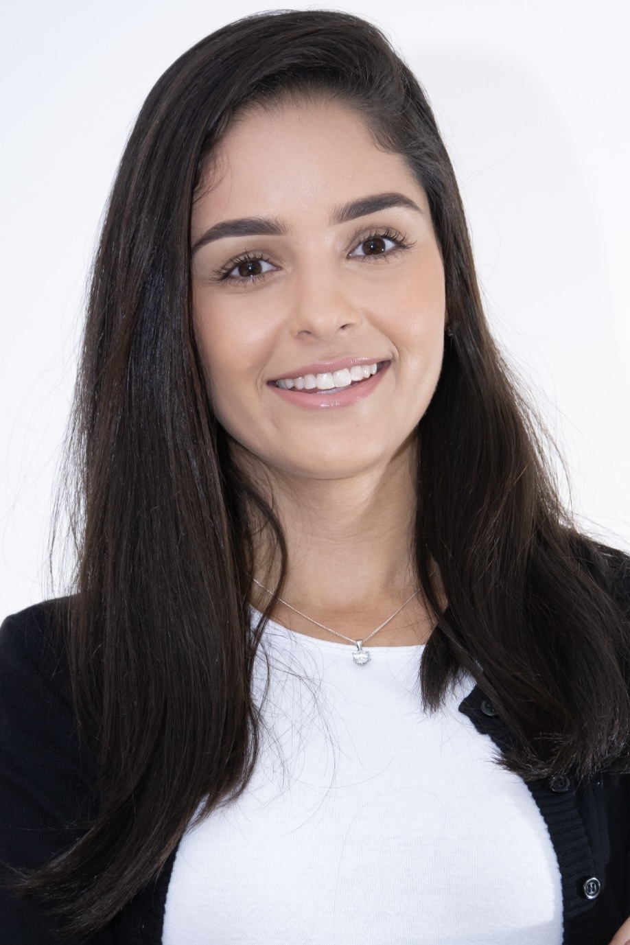 Retrato de Evelyn Souza sorrindo, com cabelo longo escuro, blusa branca e casaco preto, sobre fundo claro.
